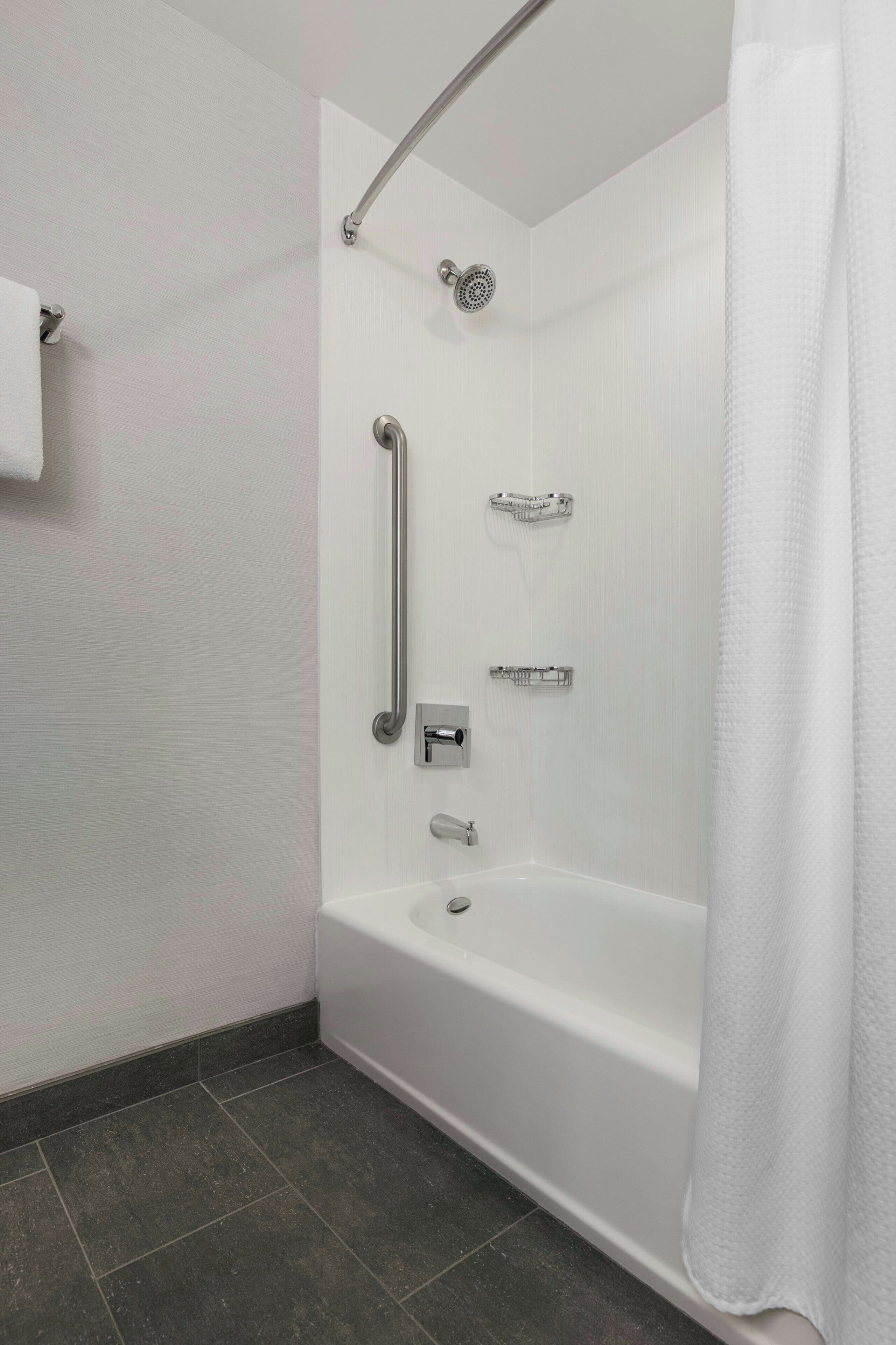 A modern bathroom with a walk-in shower, grab bars, a handheld showerhead, and a bathtub.
