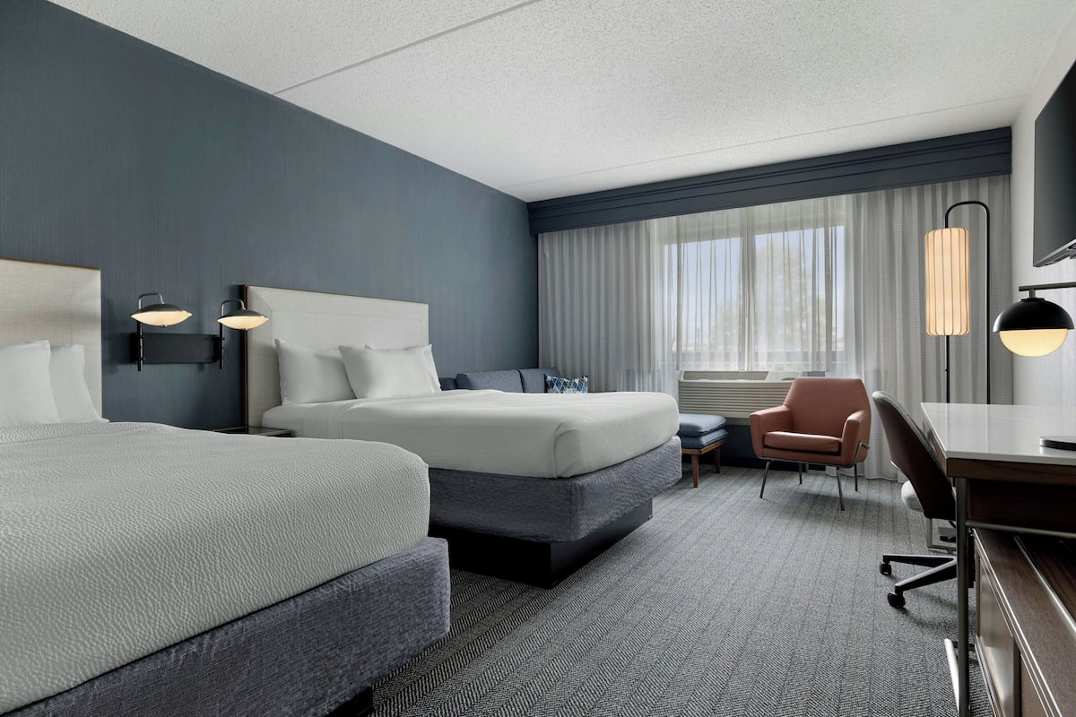 A hotel room with two beds, a desk, a chair, and a TV.