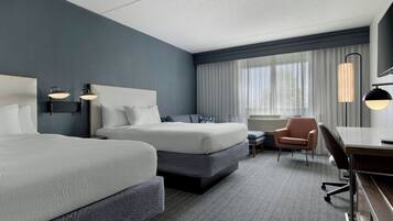 Une chambre d’hôtel avec deux lits, un bureau, une chaise et un téléviseur.