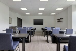 Un salón de conferencias con mesas, sillas y una pantalla grande.