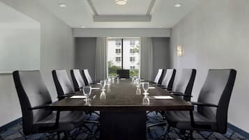 Un salón de conferencias con una larga mesa, sillas negras y vistas a un edificio a través de amplias ventanas.