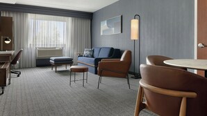 Una habitación de hotel con escritorio, sofá, silla, mesa redonda y lámpara.