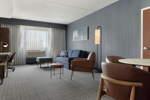 Quarto de hotel com escrivaninha, sofá, poltrona, mesa redonda e luminária.