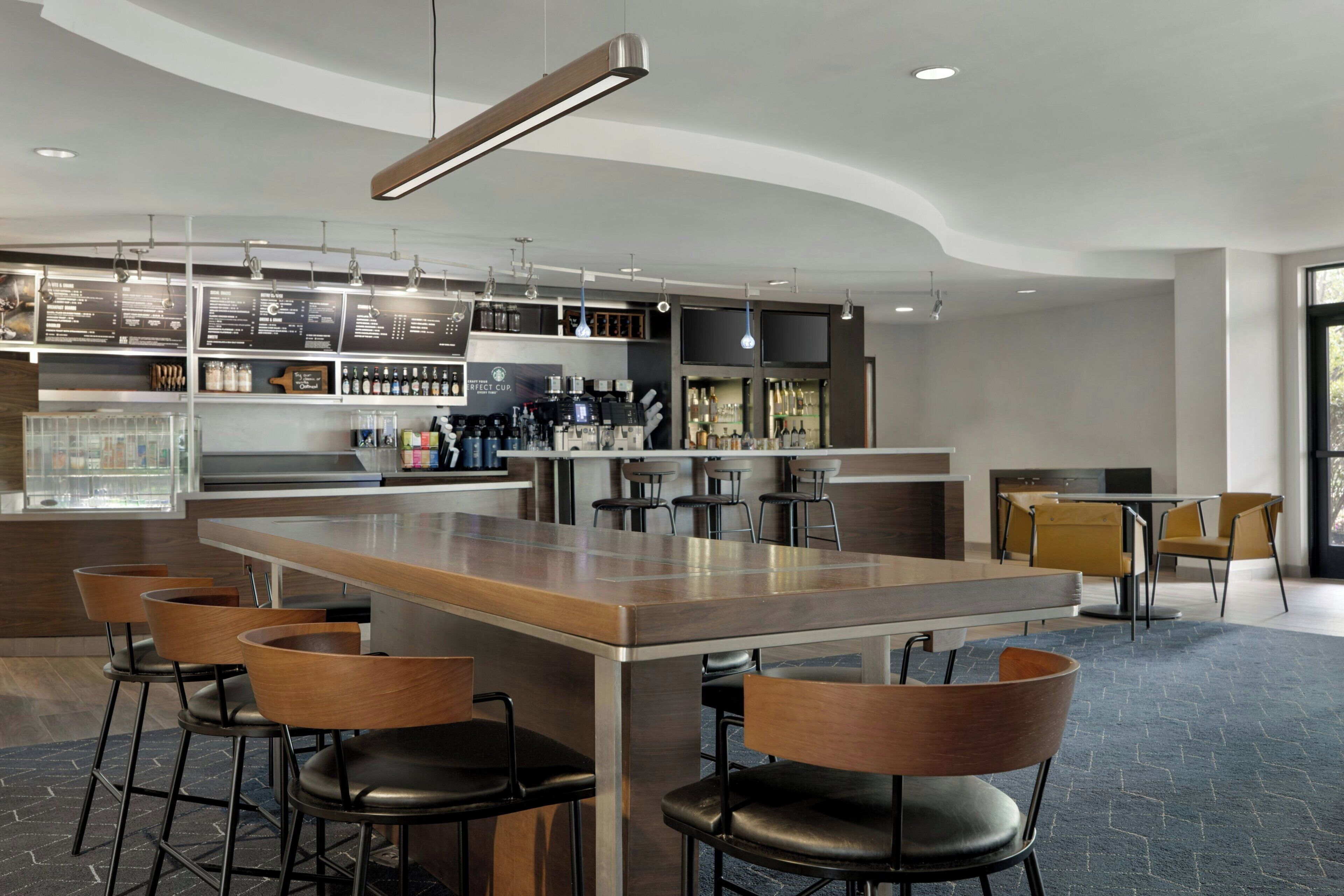 A modern bar area with a long counter, bar stools, and a variety of beverages.