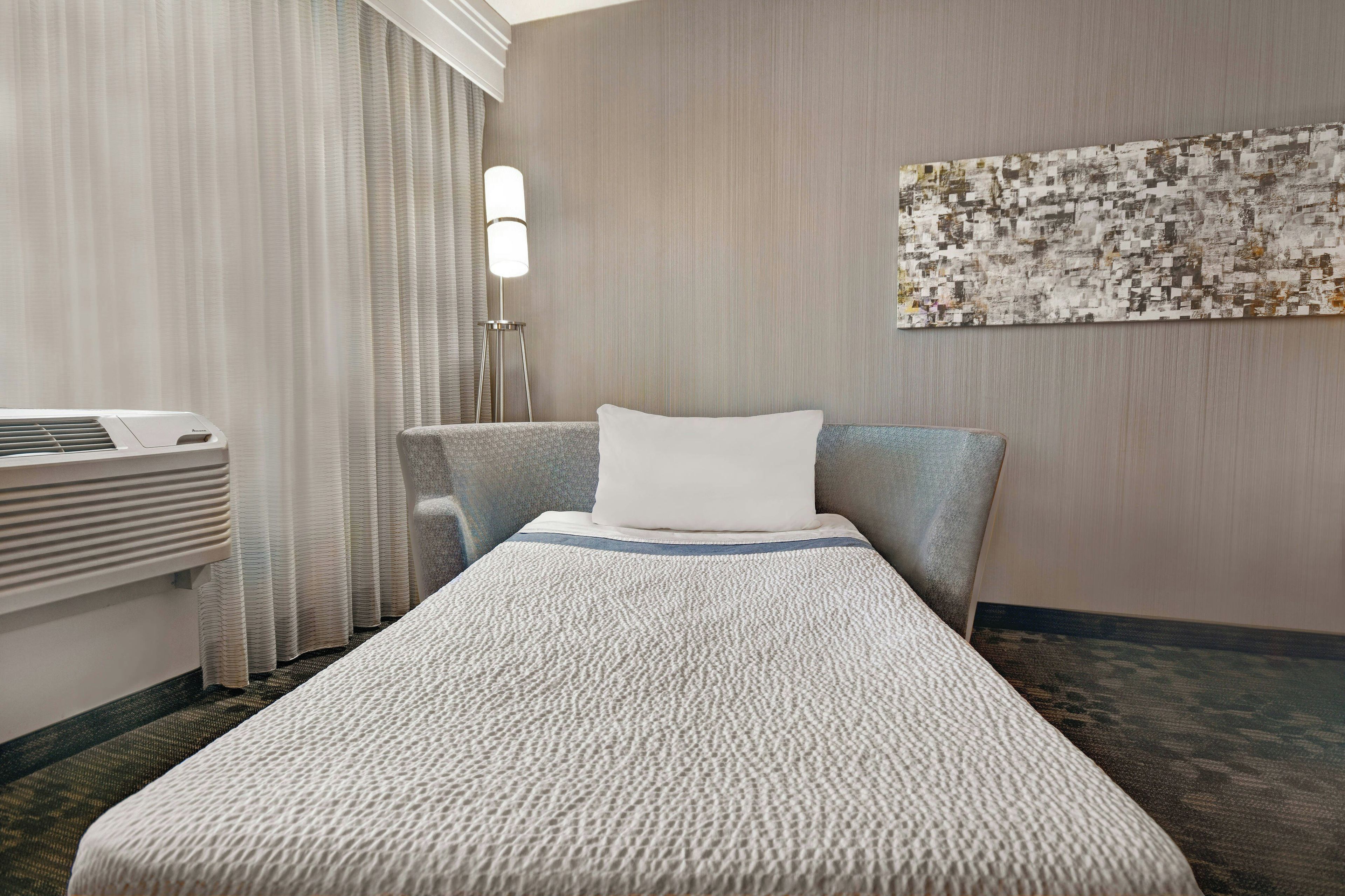 Una habitación de hotel con una cama individual, un escritorio con lámpara y una obra de arte colgada en la pared.