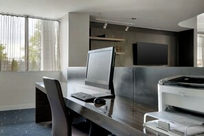 Un espacio de oficina moderno con escritorio, computadora, impresora y ventanas amplias.