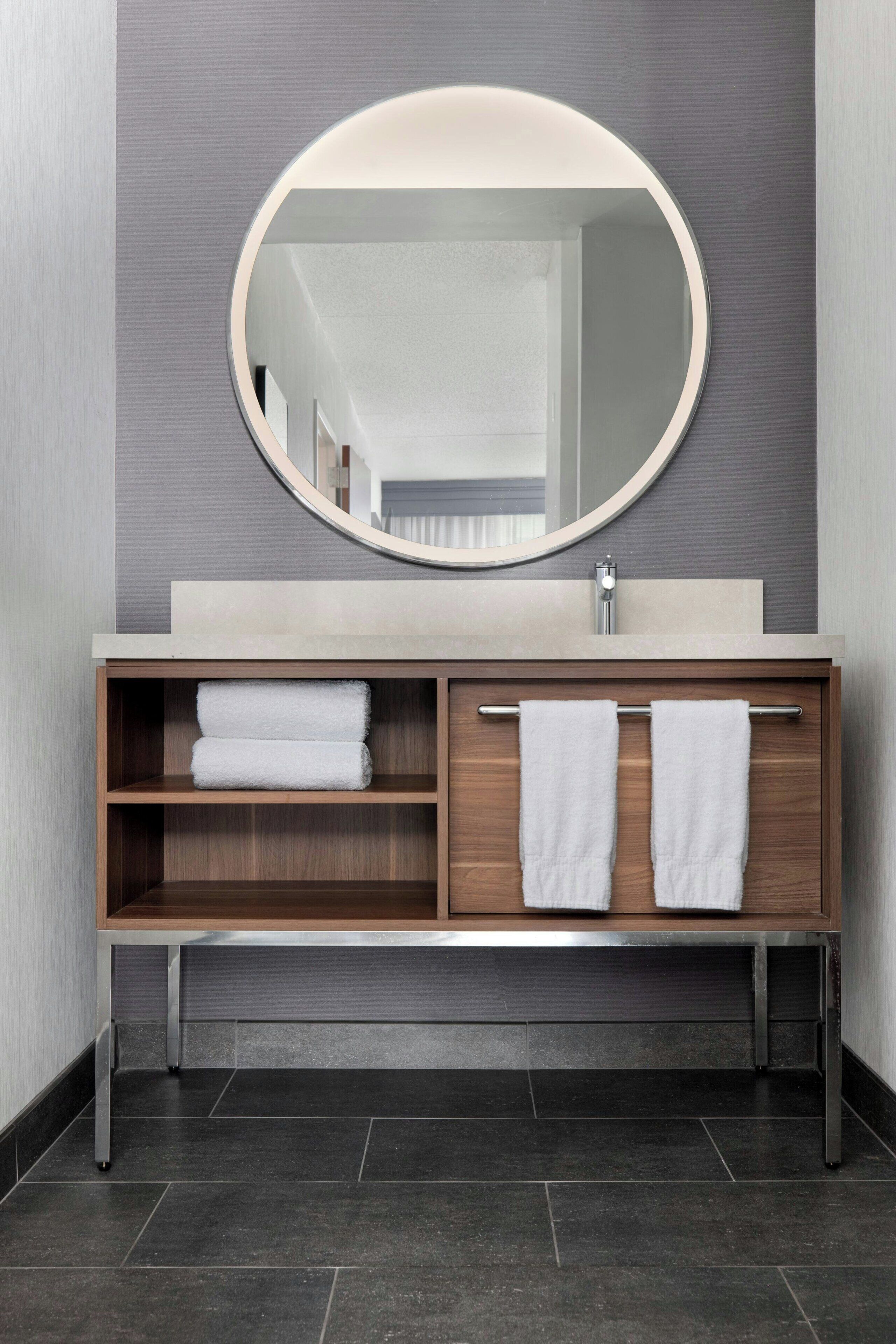 A modern bathroom with a round mirror, a beige sink, and two towels on the vanity.
