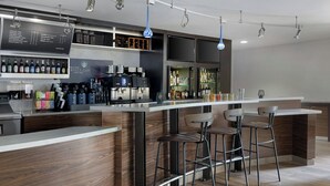 Zona de bar moderna con una máquina de café, taburetes y estantes con botellas.