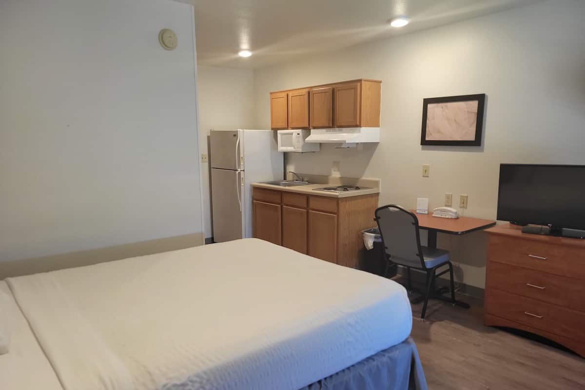 A compact room with a bed, kitchenette, desk, and TV.