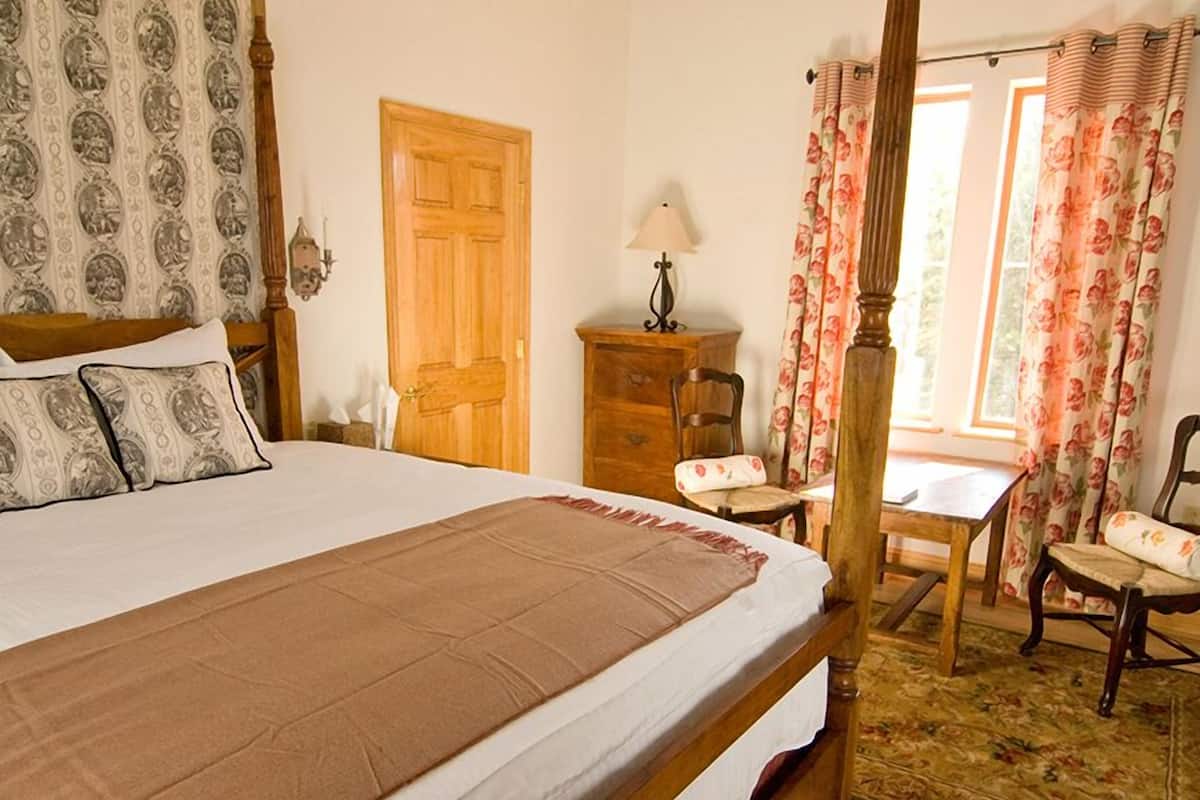 A bedroom with a large bed, wooden furniture, and a floral-patterned window treatment.
