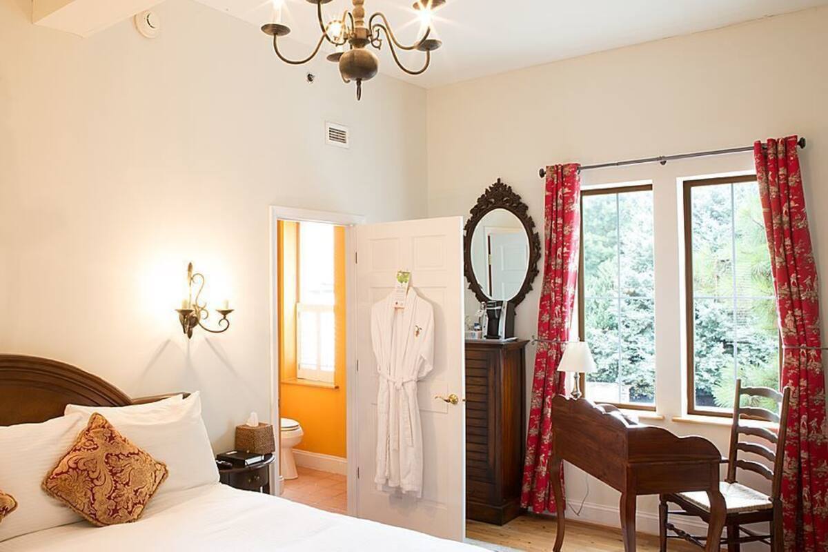 A bedroom with a wooden bed, a nightstand, a mirror, a chair, and a window with curtains.