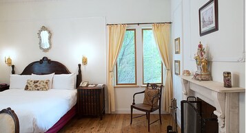 Un dormitorio con una cama grande, una silla, una chimenea y un ventanal con cortinas.