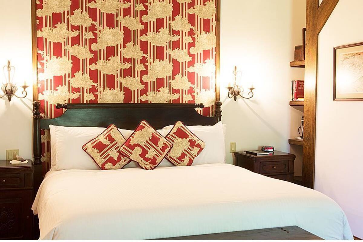 A neatly made bed with a patterned headboard, bedside tables with lamps, and a framed map on the wall.