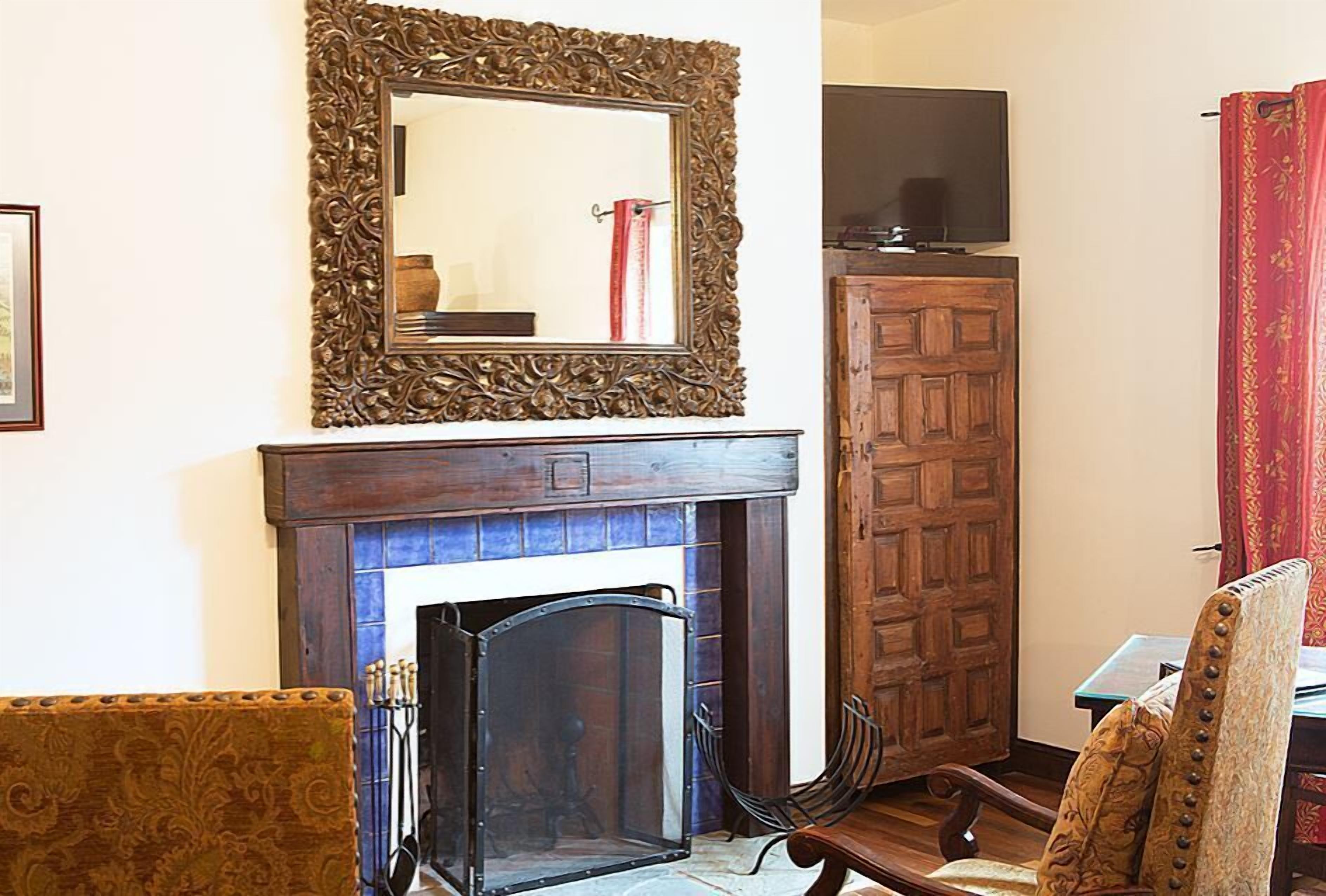 A room with a fireplace, a wooden cabinet, a television, and a patterned armchair.