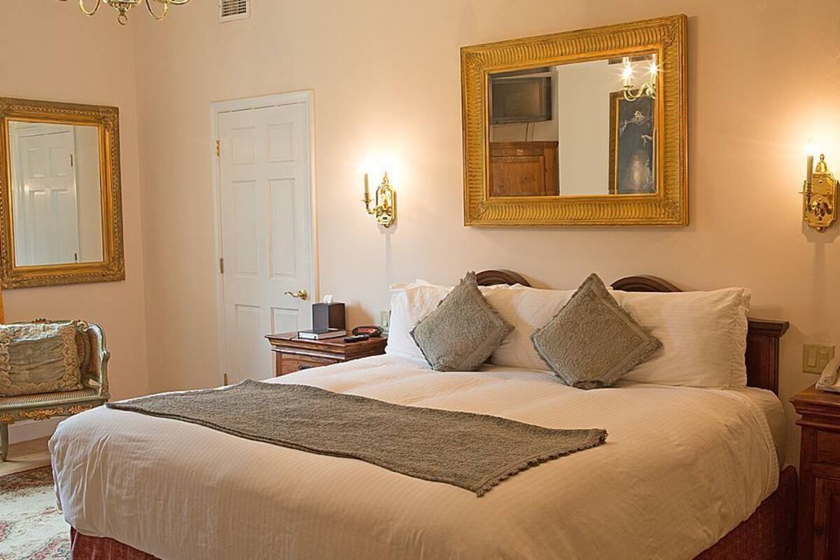A neatly arranged bedroom with a large bed, two bedside tables, a chair, a mirror, and a door.
