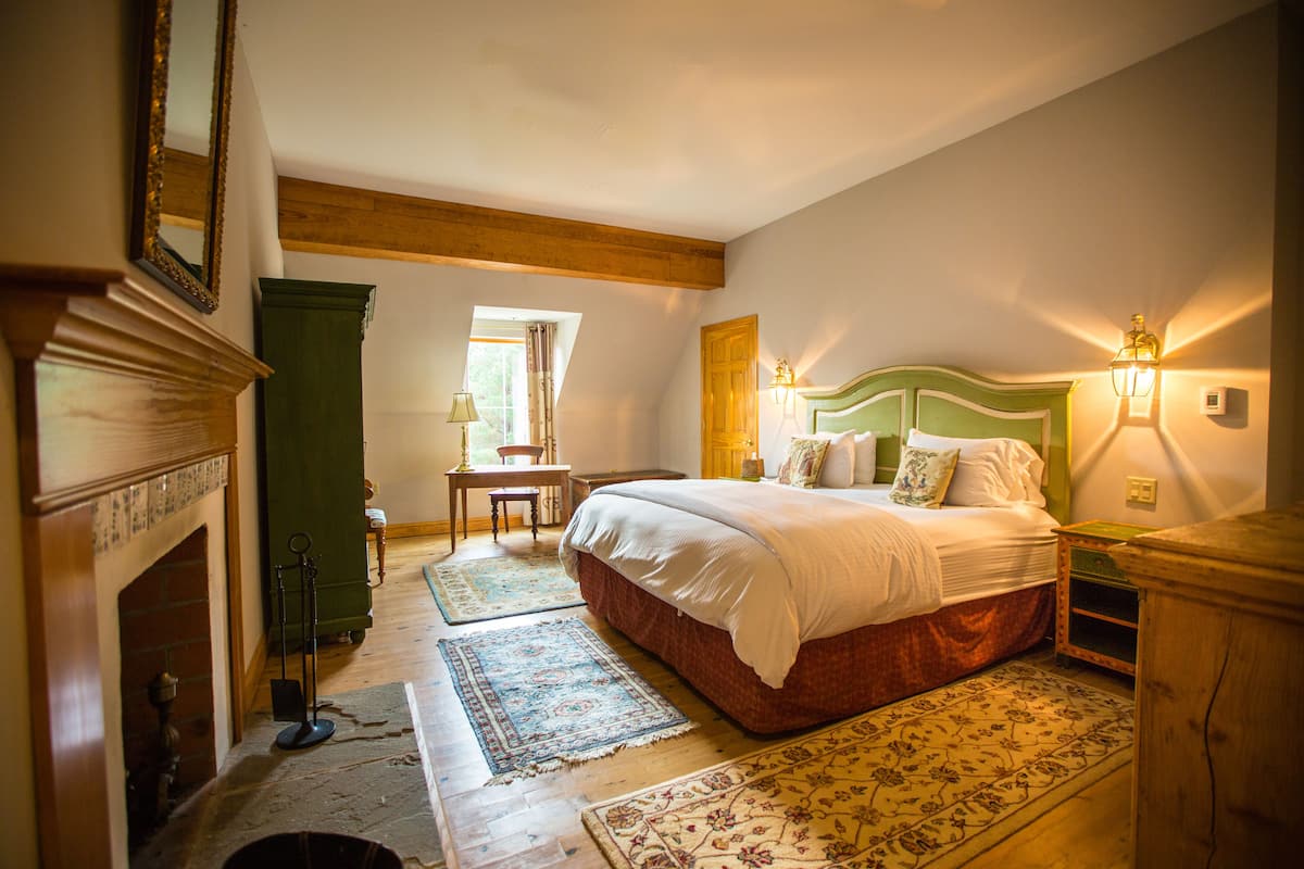 A bedroom with a large bed, a fireplace, a window, and a wooden ceiling.