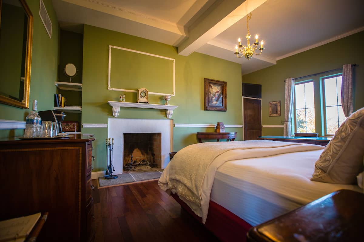 A bedroom with a large bed, a fireplace, a mirror, and a window with curtains.