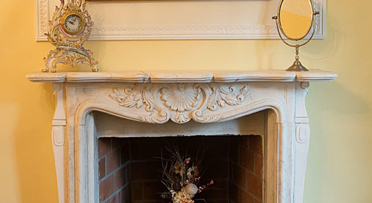 A white fireplace with intricate carvings, a clock, and a mirror above it.