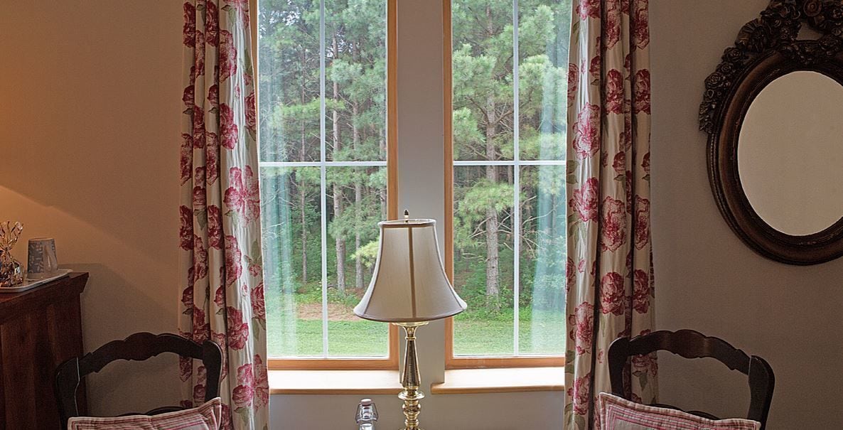 A room with a window, a lamp, two chairs, and a mirror on the wall.
