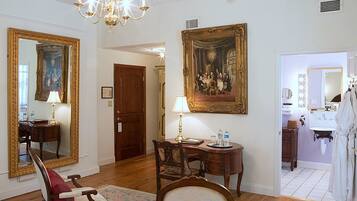A room with a wooden desk, a chair, a large mirror, and a painting on the wall.