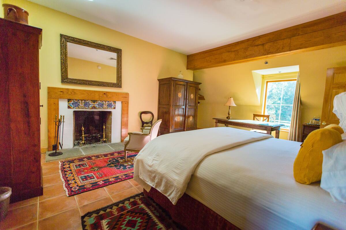 A bedroom with a large bed, a fireplace, a wooden cabinet, and a window with curtains.