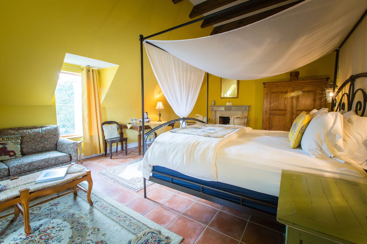 A bedroom with a four-poster bed, a sofa, a desk, and a chair.