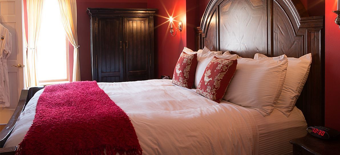 A neatly made bed with a red blanket, a wooden headboard, and floral pillows.