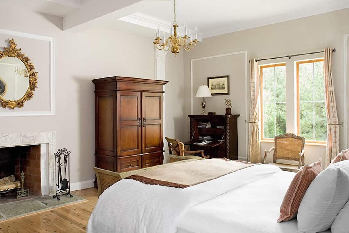 A spacious bedroom with a large bed, a wooden wardrobe, a fireplace, and a window with curtains.