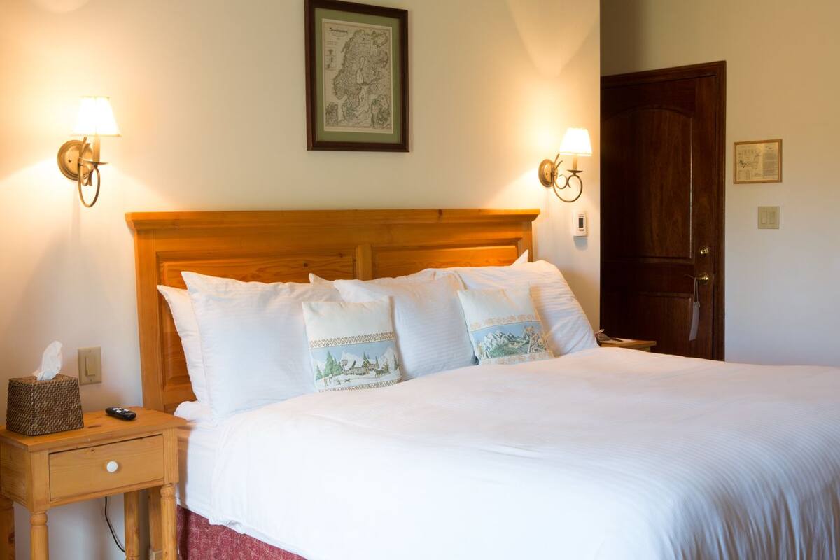 A neatly made bed with white linens and decorative pillows, a wooden headboard, bedside lamps, and a framed map on the wall.