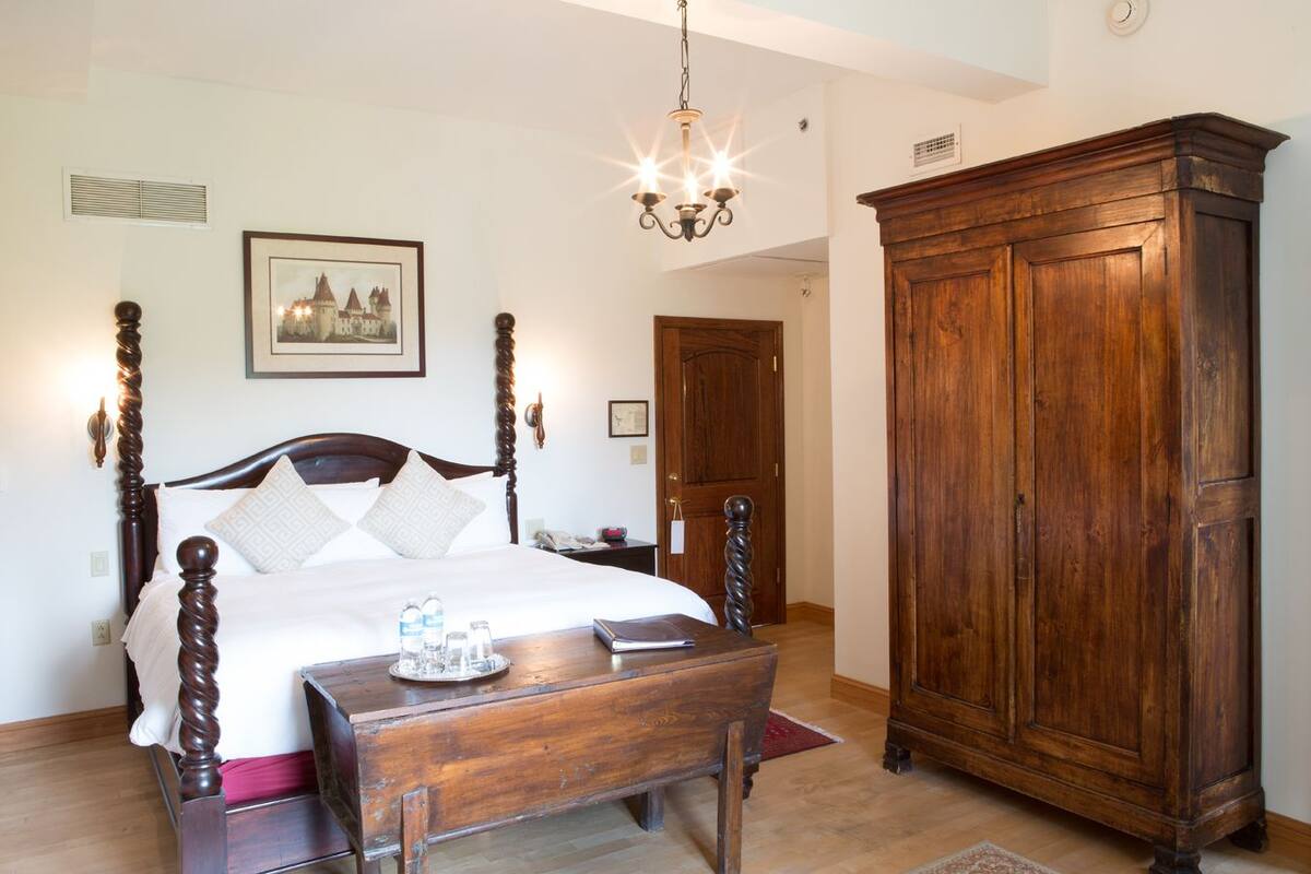A bedroom with a four-poster bed, a wooden nightstand, a wooden wardrobe, and a chandelier.