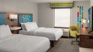 Habitación de hotel con dos camas, un escritorio, una silla y un ventanal grande.