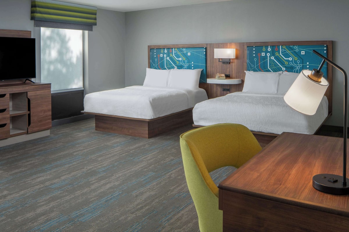 Ein Hotelzimmer mit zwei Betten, einem Fernseher, einem Schreibtisch und einem Sessel.