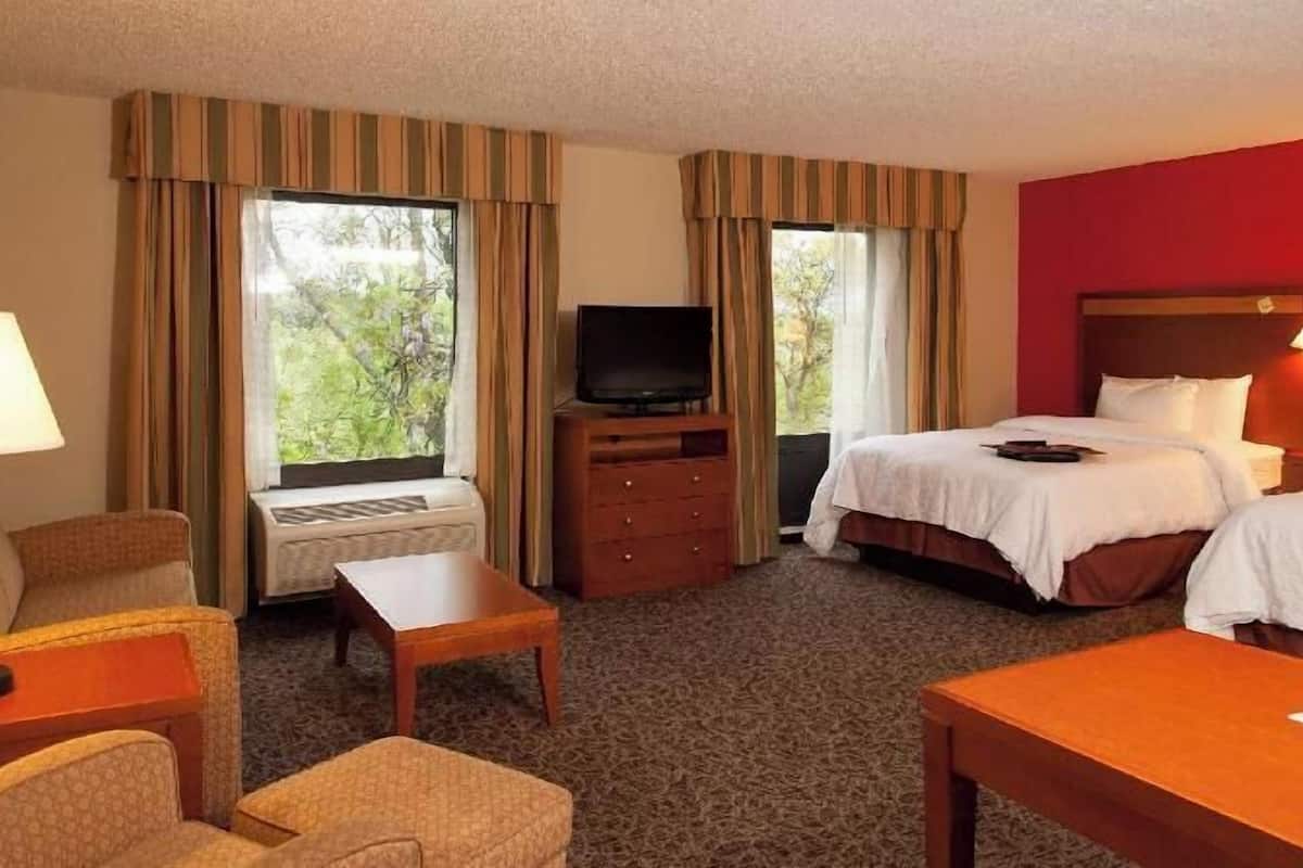 Ein Hotelzimmer mit zwei Betten, einem Fernseher, einem Schreibtisch, einem Sessel und einer Lampe.