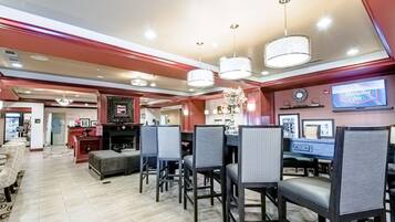 Een hotel lobby met een open haard, zithoek en een televisiescherm waarop 'Hampton Inn' staat.