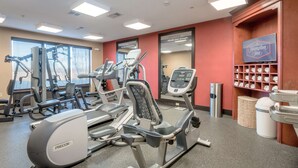 Un gimnasio con diversas máquinas de ejercicio, un letrero de Hampton Inn y un espejo que refleja la sala.