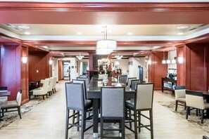 Uma ampla área de jantar com uma mesa comprida e várias cadeiras, um lustre e um espaço de bar com uma variedade de garrafas.