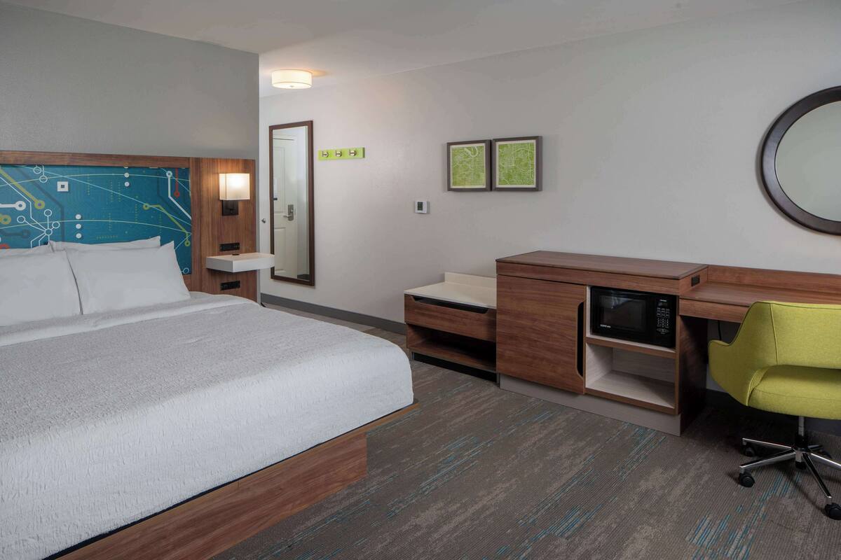 Ein Hotelzimmer mit einem großen Bett, einem Schreibtisch mit Stuhl, einer Mikrowelle und einem Spiegel.