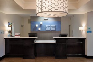 Un mostrador de recepción de hotel con un diseño moderno, que incluye un gran letrero en la pared, dos mostradores de recepción y una lámpara decorativa en el techo.