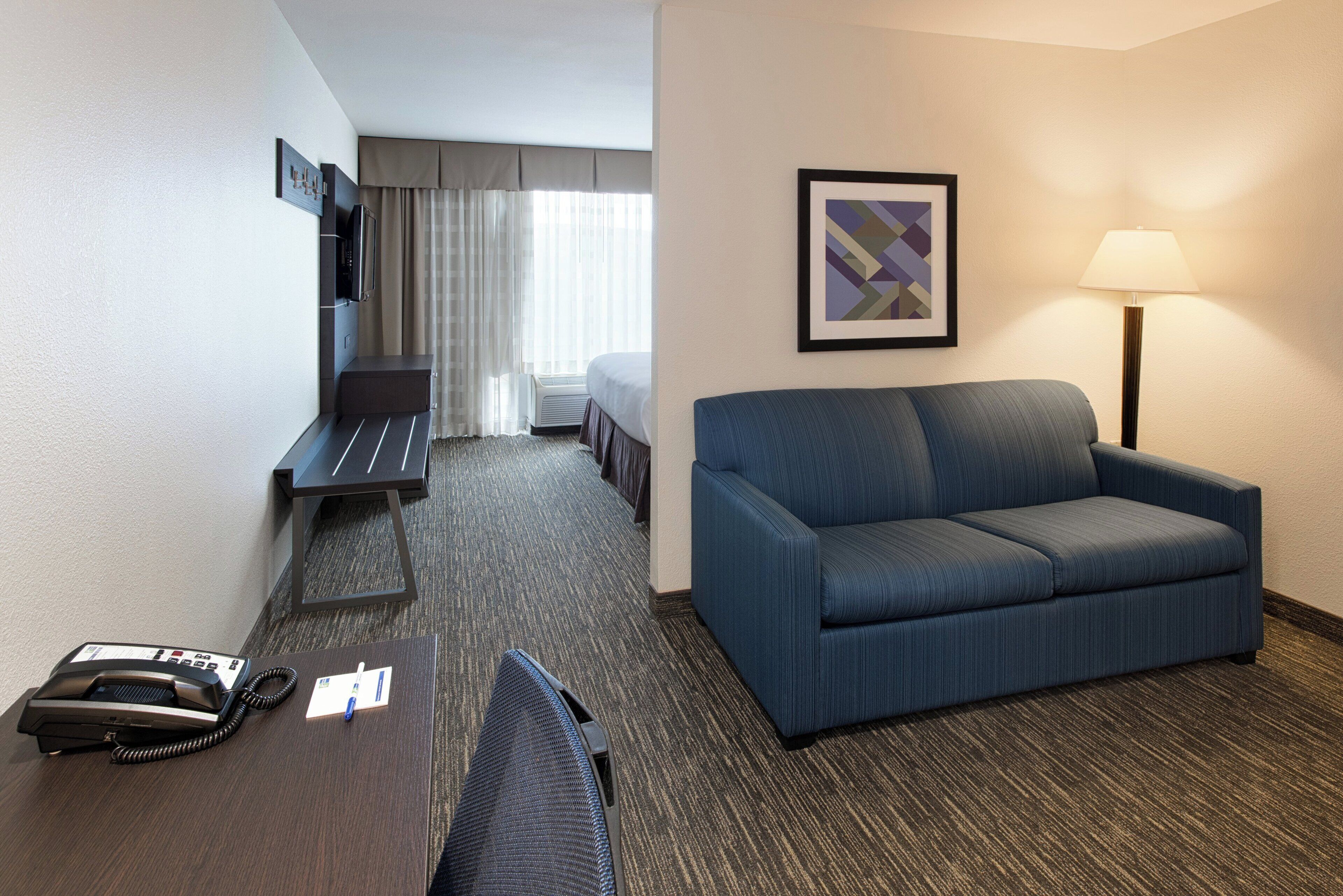 A hotel room with a bed, a desk, a chair, a sofa, a desk lamp, and a telephone.