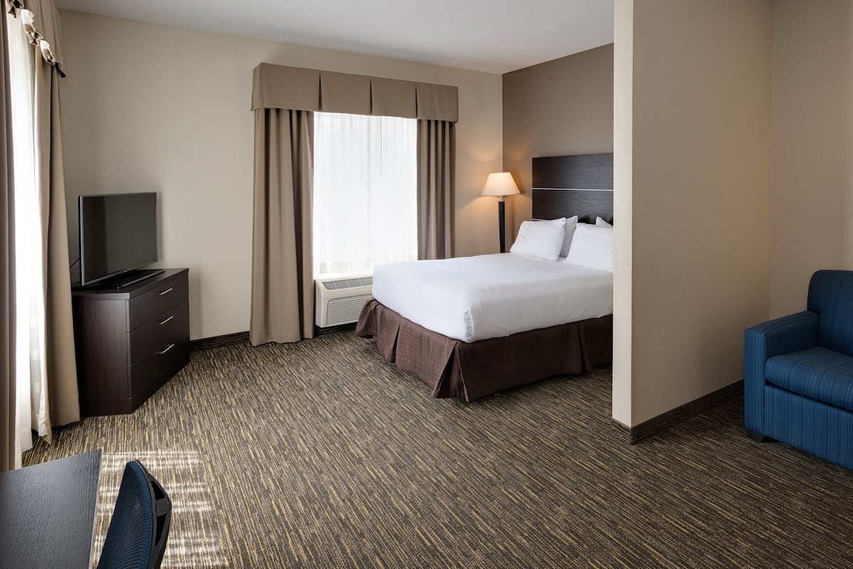 A hotel room with a bed, a TV on a dresser, a desk, and a chair.