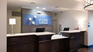 A hotel reception area with two reception desks, a blue wall with the Holiday Inn Express logo, and a modern light fixture.