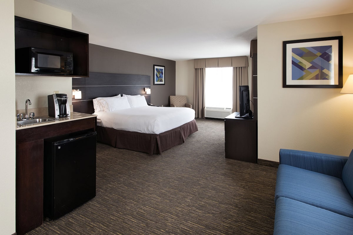 A hotel room with a bed, a desk with a microwave, a coffee maker, a TV, and a blue sofa.