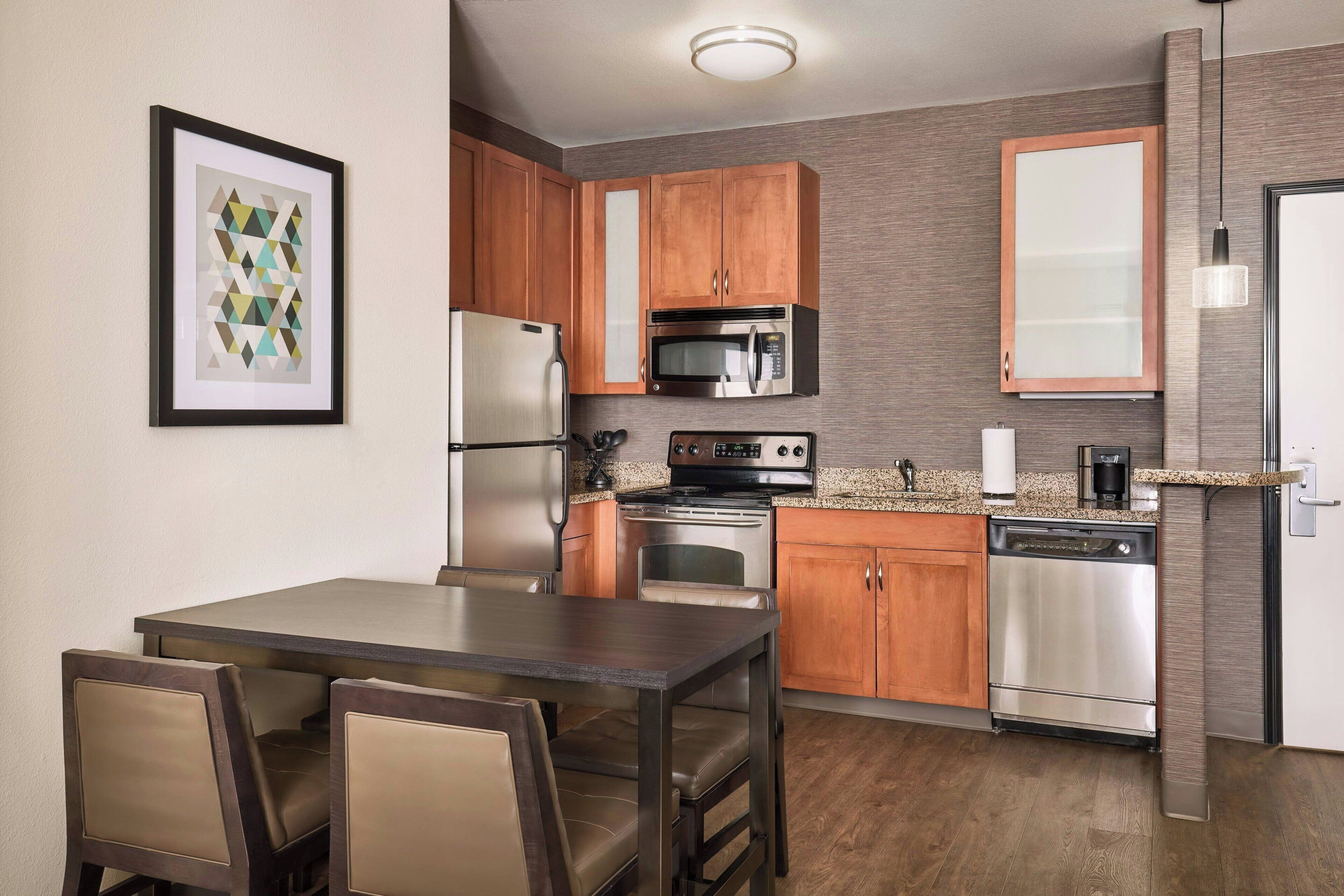 A modern kitchen with wooden cabinets, stainless steel appliances, and a dining area with a table and chairs.