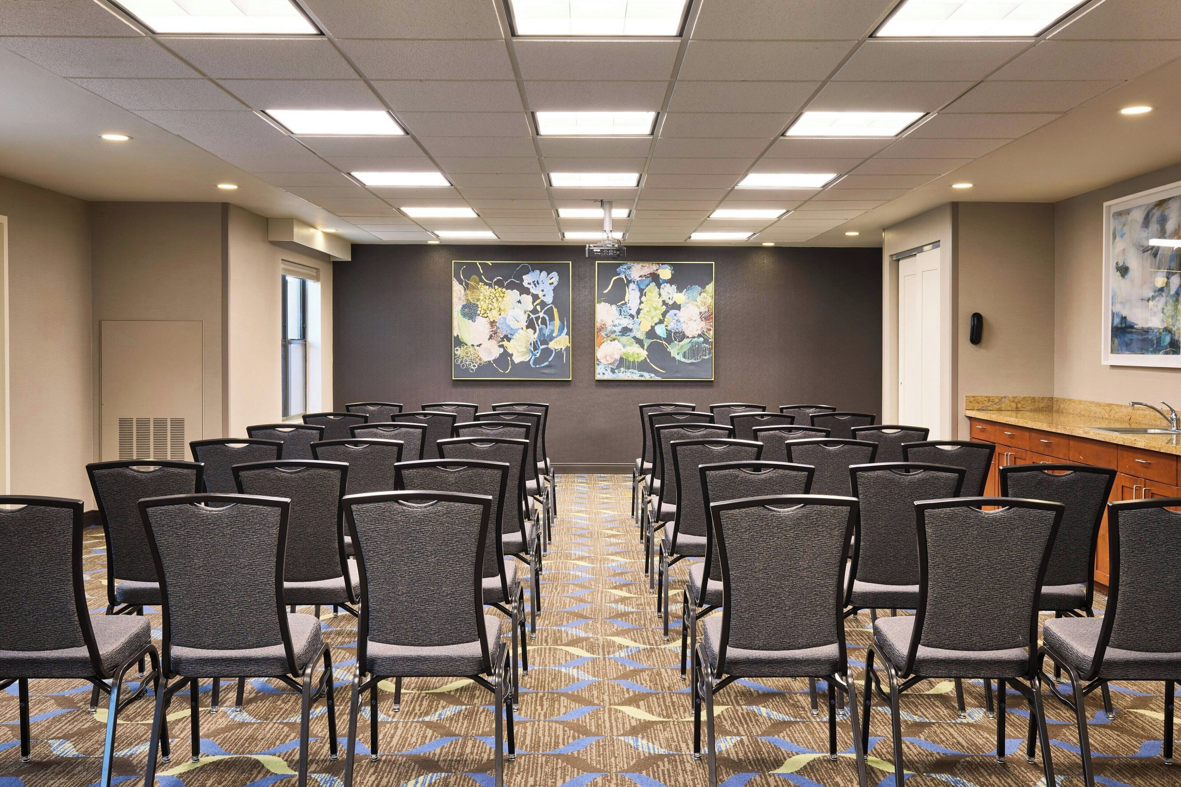 A conference room with rows of chairs, a projector screen, and two large floral paintings on the walls.