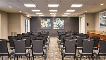 A conference room with rows of chairs, a projector screen, and two large floral paintings on the walls.