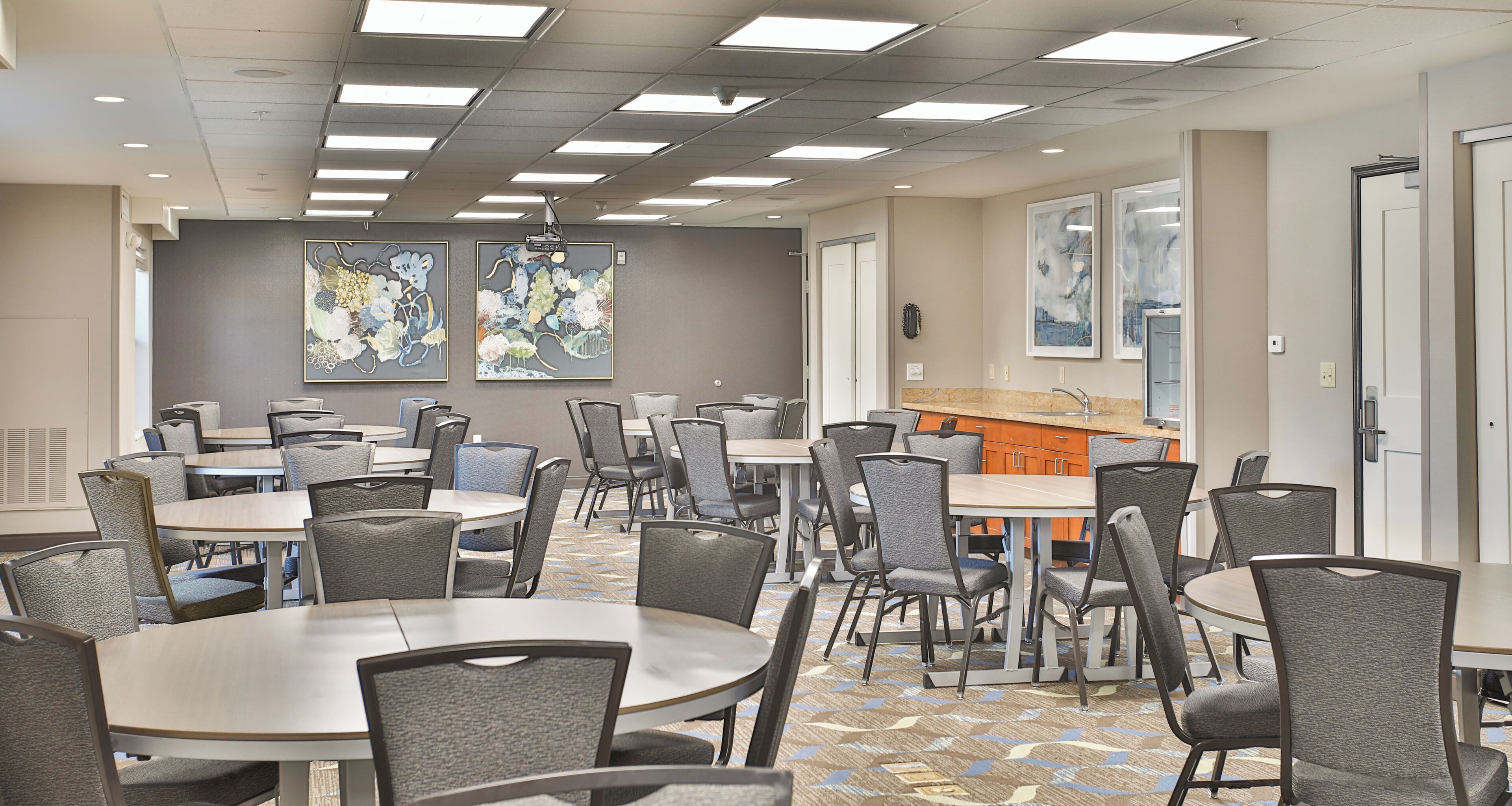 A dining area with multiple tables and chairs, a kitchen counter, and artwork on the walls.