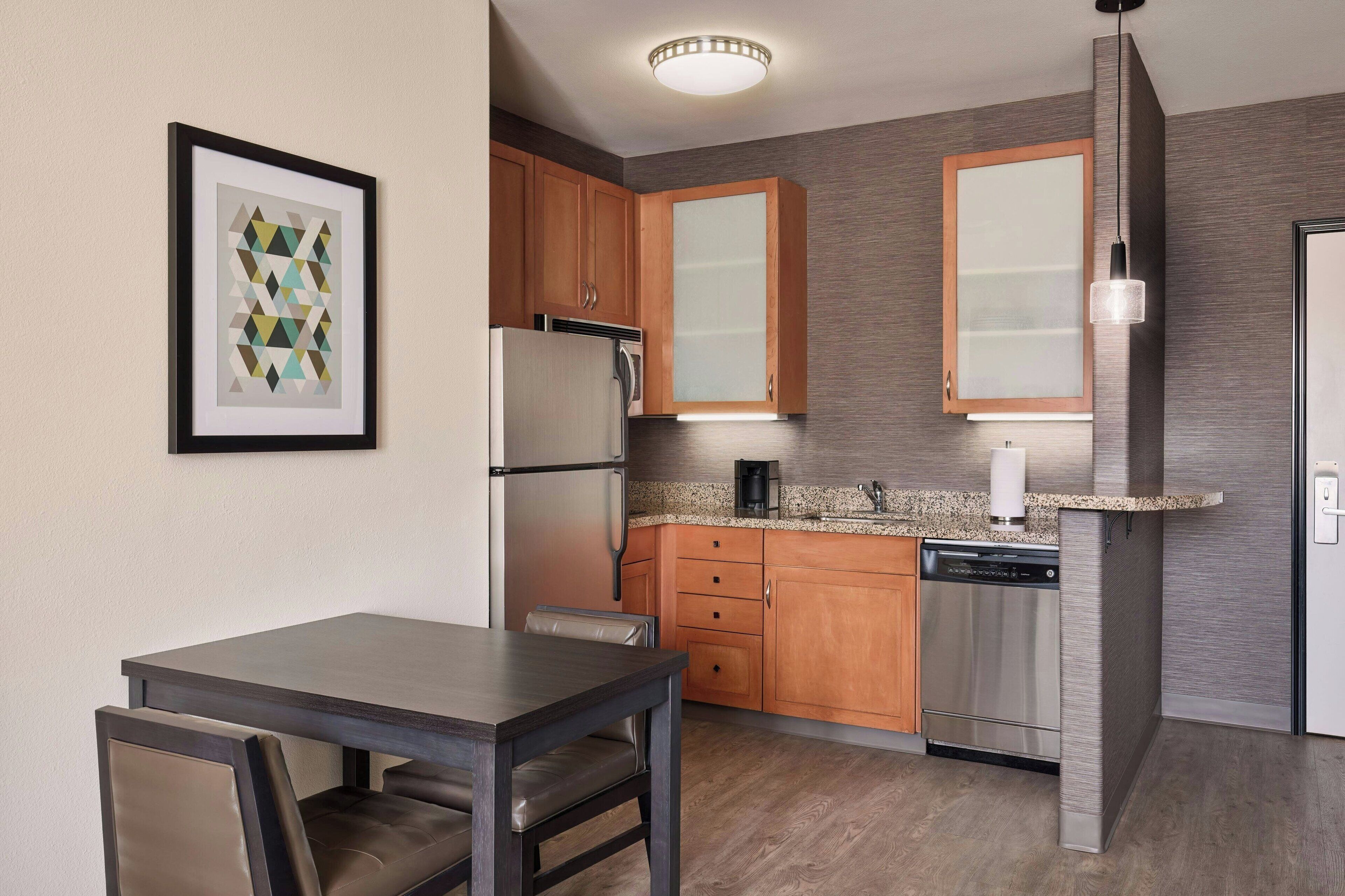A compact kitchen with wooden cabinets, a stainless steel refrigerator, and a dishwasher.