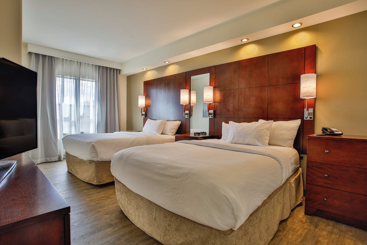A hotel room with two beds, a TV, a wooden dresser, and a large mirror.