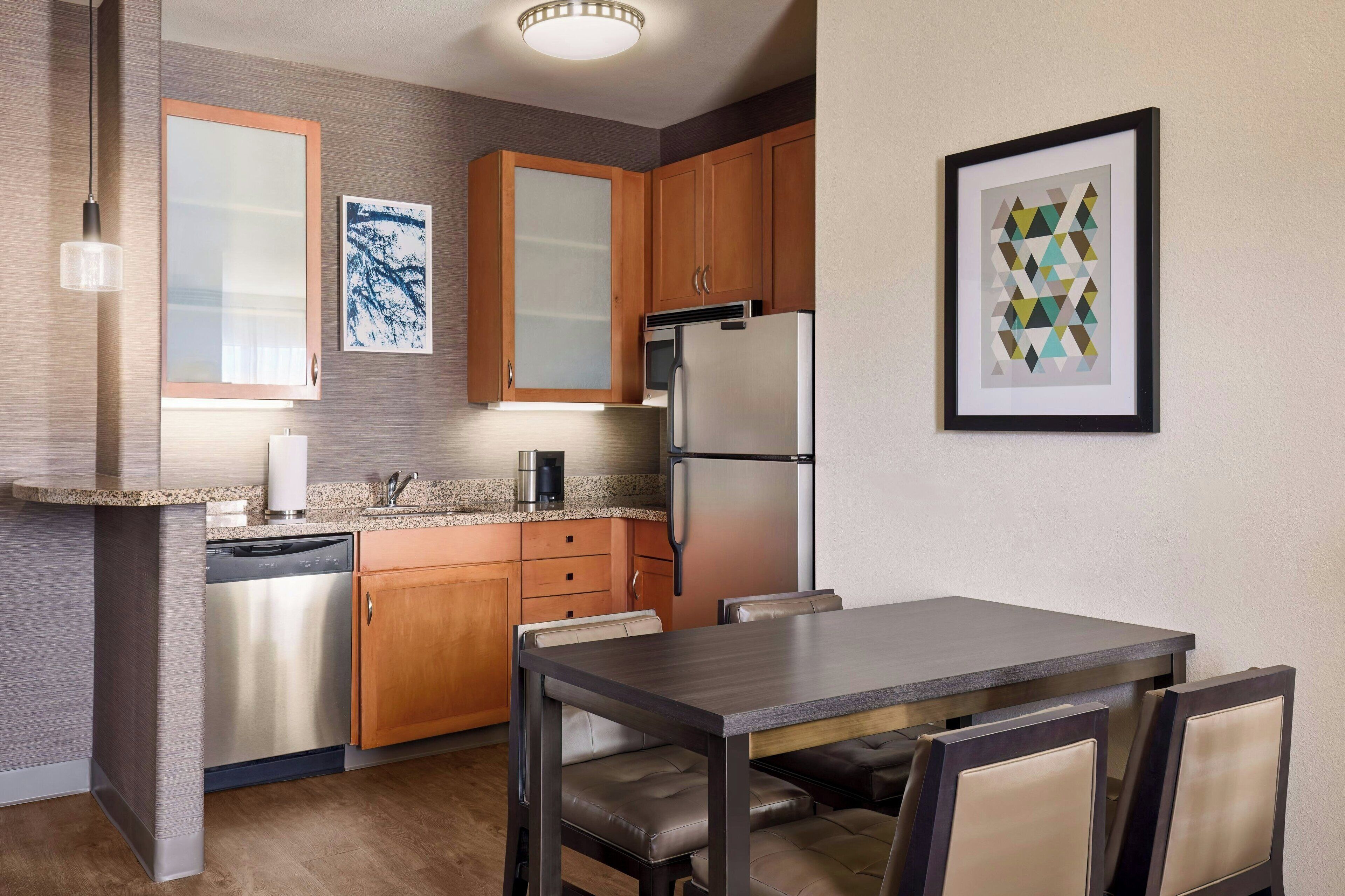 A modern kitchen with wooden cabinets, stainless steel appliances, and a dining area with a dark wood table and cushioned chairs.
