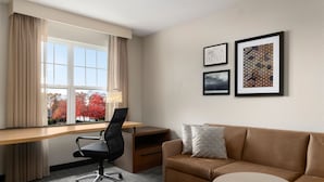 A hotel room with a desk, a black office chair, a brown sofa, a small round table, and three framed pictures on the wall. - Residence Inn by Marriott Neptune at Gateway Center (Neptune City)